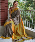 Woman in a yellow and gray saree sitting on a balcony with greenery in the background
